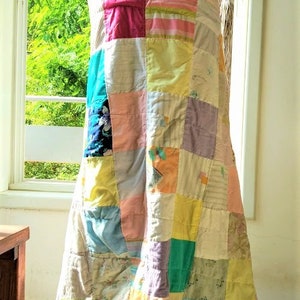 May include: A patchwork quilt made from various fabrics in shades of pink, yellow, green, blue, and purple. The quilt is folded and draped over a person's shoulders.