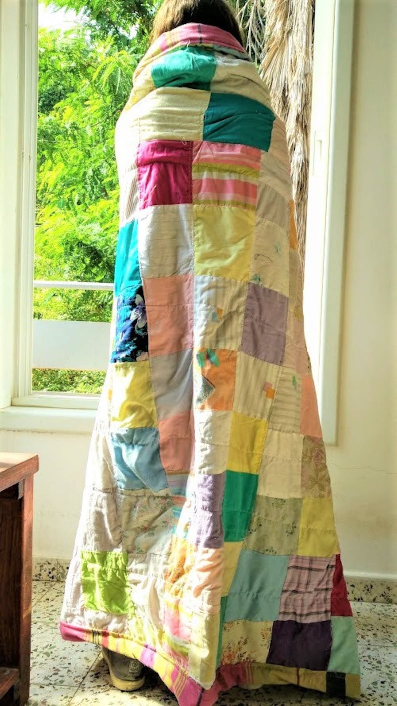 May include: A patchwork quilt made from various fabrics in shades of pink, yellow, green, blue, and purple. The quilt is folded and draped over a person's shoulders.