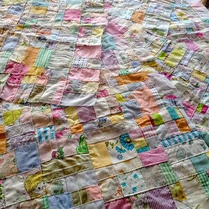 May include: A patchwork quilt made of various fabrics in shades of pink, yellow, blue, and green. The quilt is made up of small squares sewn together to create a larger pattern.