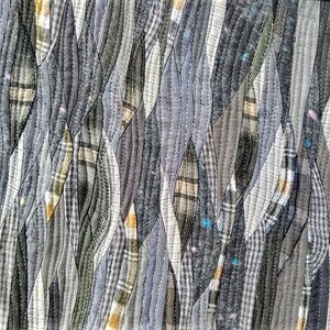 Może przedstawiać: Abstrakcyjne dzieło sztuki tekstylnej z patchworkowym wzorem. Składa się z pask&oacute;w tkaniny w odcieniach szarości, czerni i bieli, z wzorami w kratę i paski. Paski są zszyte widocznymi szwami, tworząc teksturowaną powierzchnię.