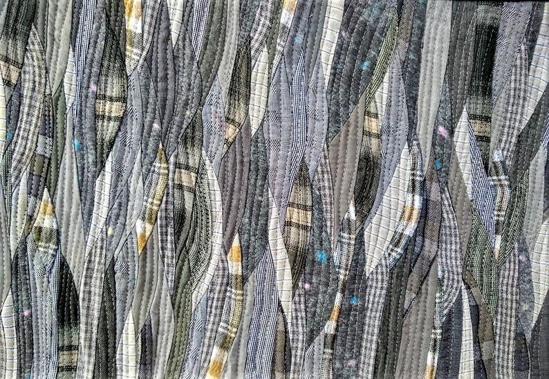 Może przedstawiać: Abstrakcyjne dzieło sztuki tekstylnej z patchworkowym wzorem. Składa się z pask&oacute;w tkaniny w odcieniach szarości, czerni i bieli, z wzorami w kratę i paski. Paski są zszyte widocznymi szwami, tworząc teksturowaną powierzchnię.