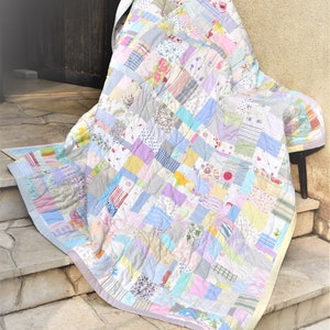 May include: A patchwork quilt made from a variety of fabrics in pastel colors, including pink, blue, yellow, and green. The quilt is folded and draped over a chair on a set of stone steps.
