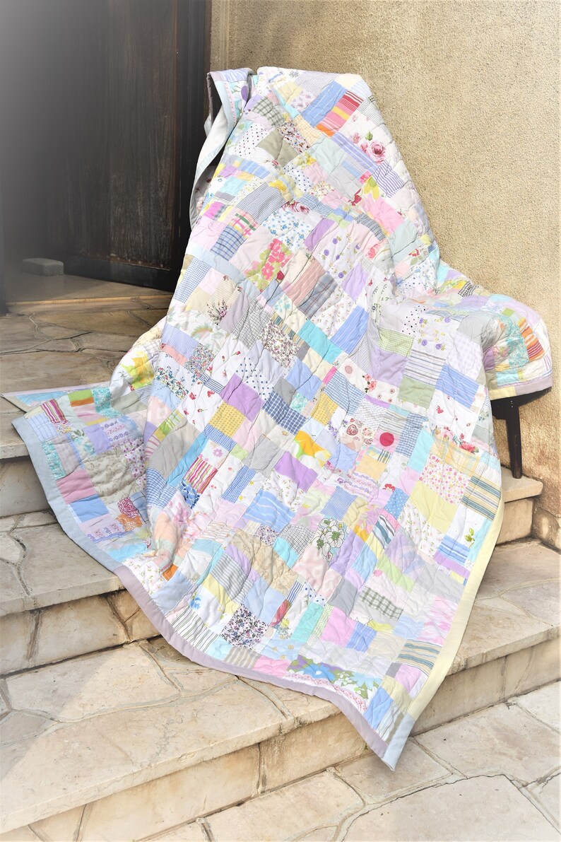 May include: A patchwork quilt made from a variety of fabrics in pastel colors, including pink, blue, yellow, and green. The quilt is folded and draped over a chair on a set of stone steps.