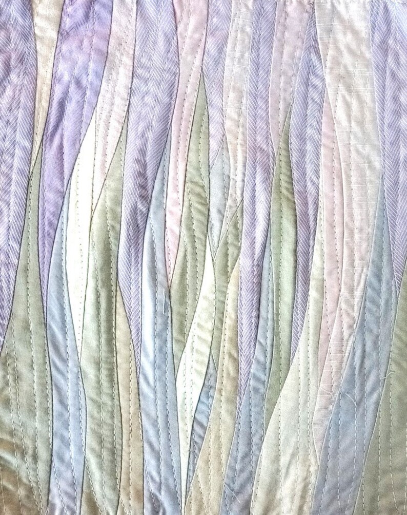 May include: A quilted fabric wall hanging with a wavy pattern in shades of purple, green, and blue.