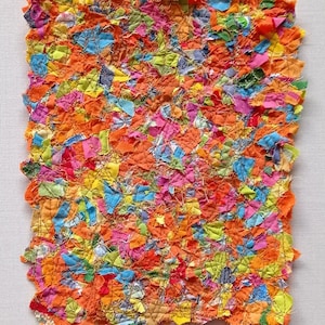 May include: A colourful patchwork textile art piece with a variety of bright colours, including orange, pink, yellow, blue, and green. The fabric is cut into small pieces and sewn together to create a textured surface.