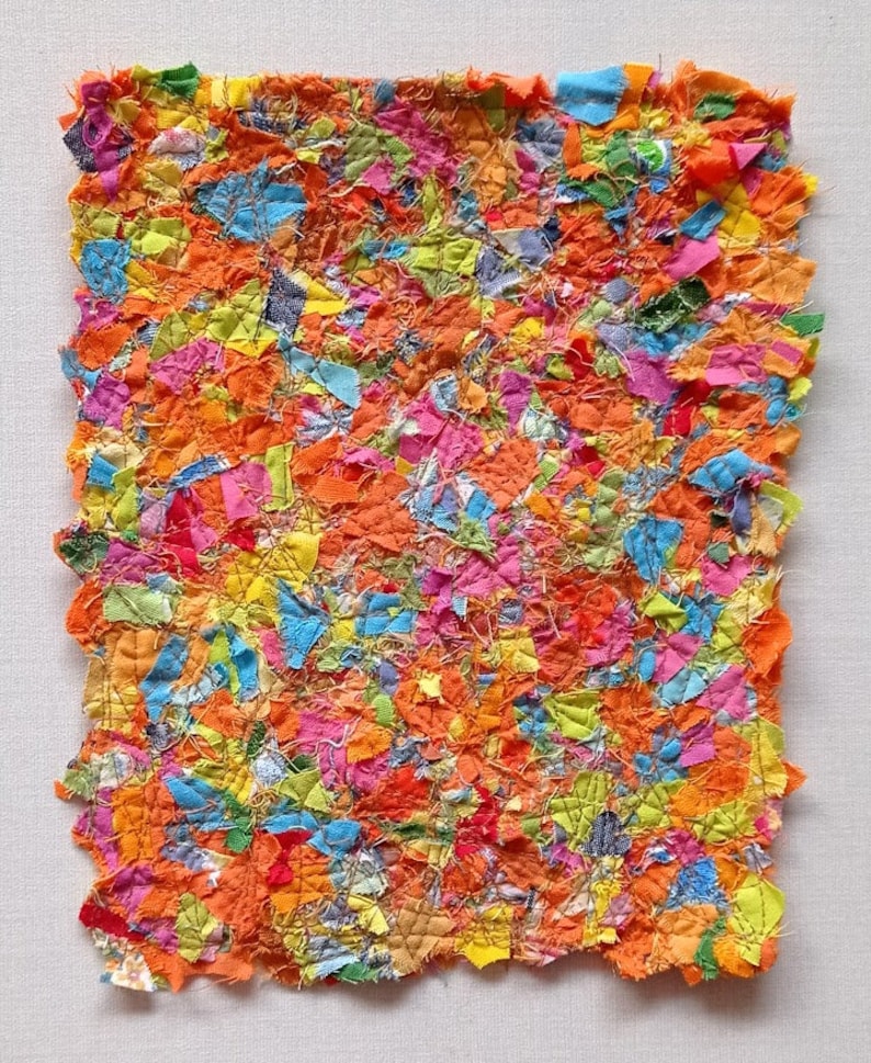 May include: A colourful patchwork textile art piece with a variety of bright colours, including orange, pink, yellow, blue, and green. The fabric is cut into small pieces and sewn together to create a textured surface.