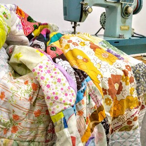May include: A vintage blue sewing machine with a foot pedal and a colourful patchwork quilt draped over it.