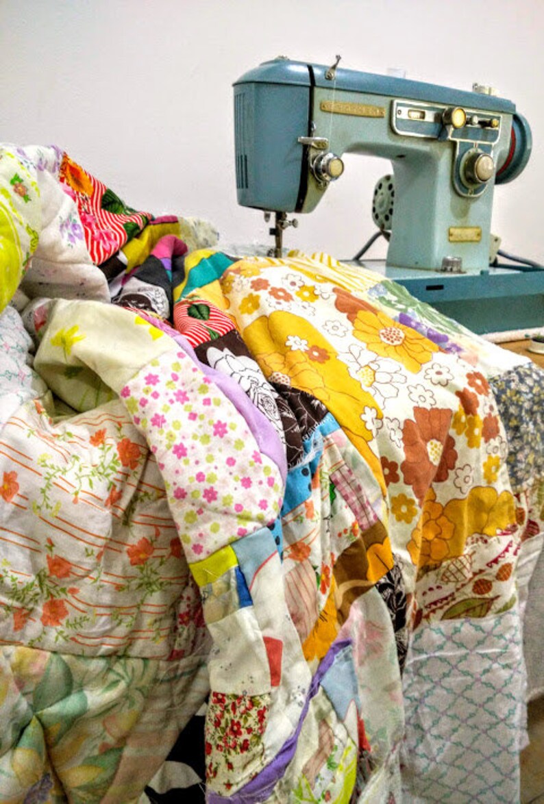 May include: A vintage blue sewing machine with a foot pedal and a colourful patchwork quilt draped over it.