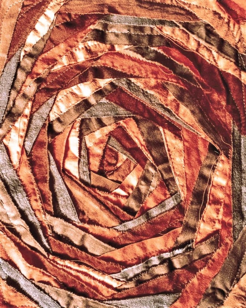 Pu&ograve; includere: Un primo piano di un'opera d'arte tessile circolare realizzata con strisce di tessuto in tonalit&agrave; di marrone, arancione e beige. Il tessuto &egrave; cucito a spirale, creando un effetto testurizzato e tridimensionale.