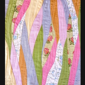 May include: A patchwork quilt with a wavy design featuring various floral patterns in shades of pink, green, yellow, and blue.