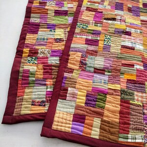 May include: Two patchwork quilt table runners with a burgundy border. The runners are made of various fabrics in shades of orange, brown, purple, green, and pink.
