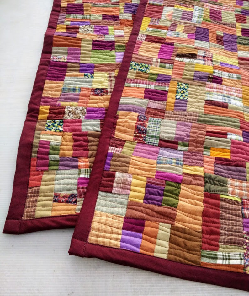 May include: Two patchwork quilt table runners with a burgundy border. The runners are made of various fabrics in shades of orange, brown, purple, green, and pink.