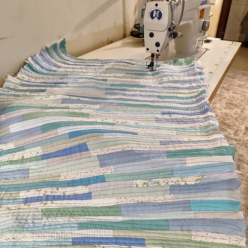 Puede incluir: Primer plano de una colcha de retazos azul y verde que se cose en una m&aacute;quina de coser. La colcha est&aacute; hecha de muchas telas diferentes, y las costuras son visibles.