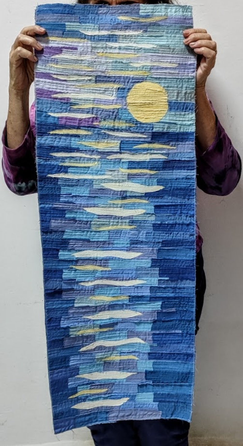 May include: A long, rectangular wall hanging made of fabric with a blue, white and yellow abstract design. The design features a large yellow circle in the centre, surrounded by white and blue lines.