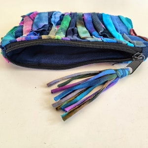 Puede incluir: Una peque&ntilde;a bolsa con cremallera hecha de retazos de tela de colores. La bolsa tiene una cremallera negra y un borla hecha de los mismos retazos de tela.