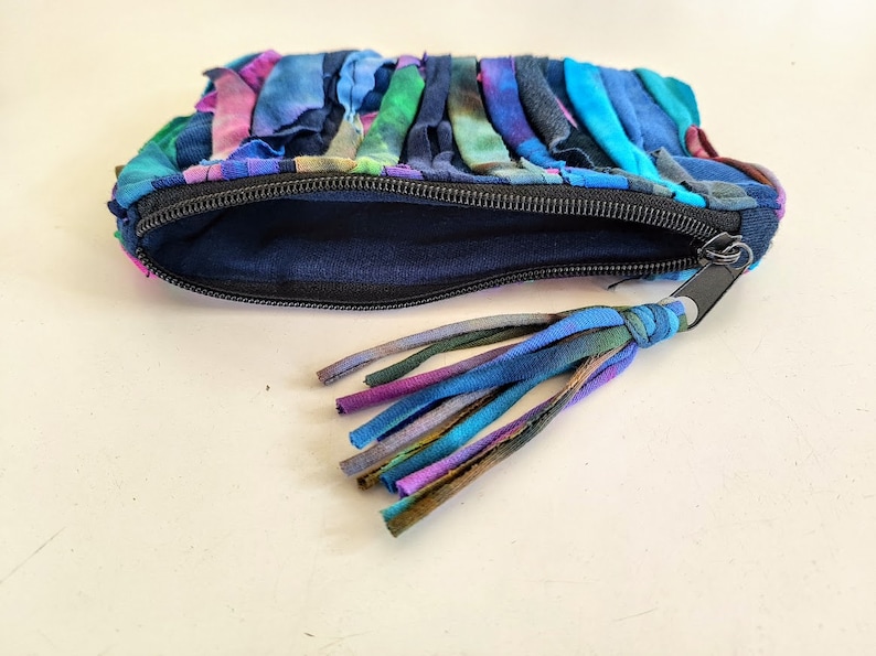 Puede incluir: Una peque&ntilde;a bolsa con cremallera hecha de retazos de tela de colores. La bolsa tiene una cremallera negra y un borla hecha de los mismos retazos de tela.