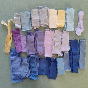 May include: A collection of fabric scraps in various shades of blue, purple, and yellow. The fabric scraps are arranged in a gradient pattern, starting with the lightest shade of blue at the top and transitioning to the darkest shade of blue at the bottom.