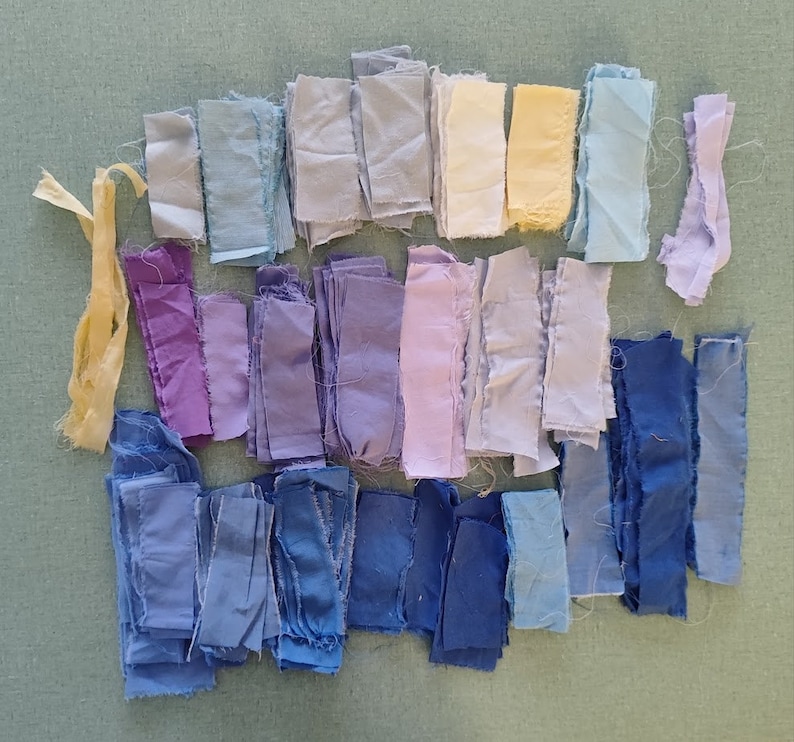 May include: A collection of fabric scraps in various shades of blue, purple, and yellow. The fabric scraps are arranged in a gradient pattern, starting with the lightest shade of blue at the top and transitioning to the darkest shade of blue at the bottom.