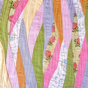 May include: A patchwork quilt with a wavy design featuring various floral patterns in shades of pink, green, blue, and yellow.