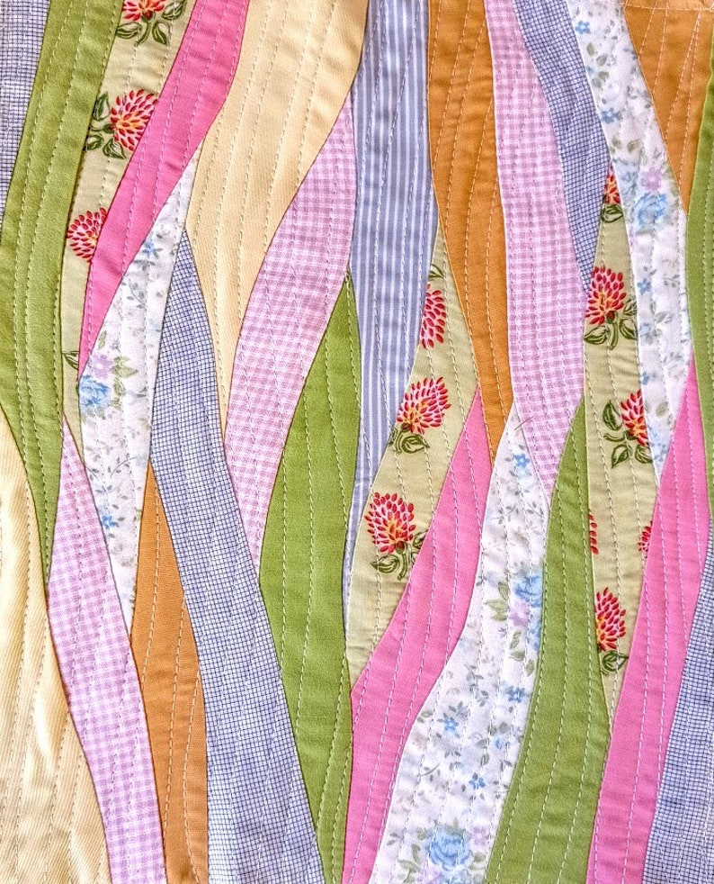 May include: A patchwork quilt with a wavy design featuring various floral patterns in shades of pink, green, blue, and yellow.
