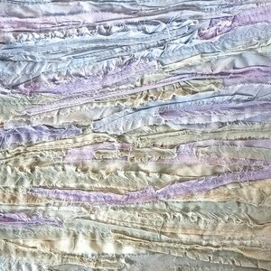 May include: A close-up of a textured fabric made of strips of light blue, lavender, and beige fabric sewn together.