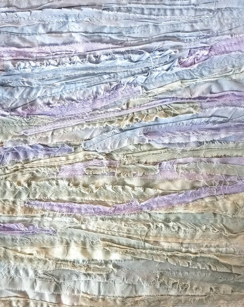 May include: A close-up of a textured fabric made of strips of light blue, lavender, and beige fabric sewn together.