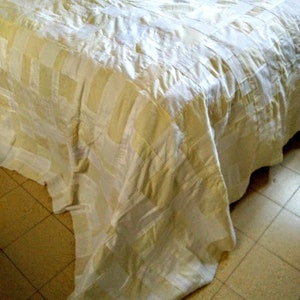 Puede incluir: Un cubrecama a rayas blancas y crema con un patr&oacute;n texturizado. El cubrecama est&aacute; hecho de una tela suave y lujosa.