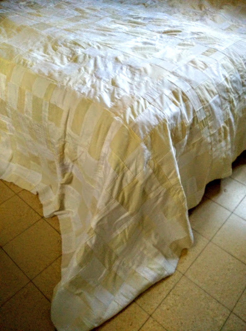 Puede incluir: Un cubrecama a rayas blancas y crema con un patr&oacute;n texturizado. El cubrecama est&aacute; hecho de una tela suave y lujosa.