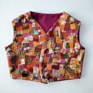 Op de afbeelding: Een patchwork vest met een bordeauxvoering. Het vest is gemaakt van veel verschillende stoffen in tinten bruin, oranje, groen, paars en roze.