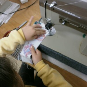 May include: A person is using a sewing machine to sew a piece of fabric. The fabric is colorful and has a floral pattern. The sewing machine is brown and has a white foot pedal.