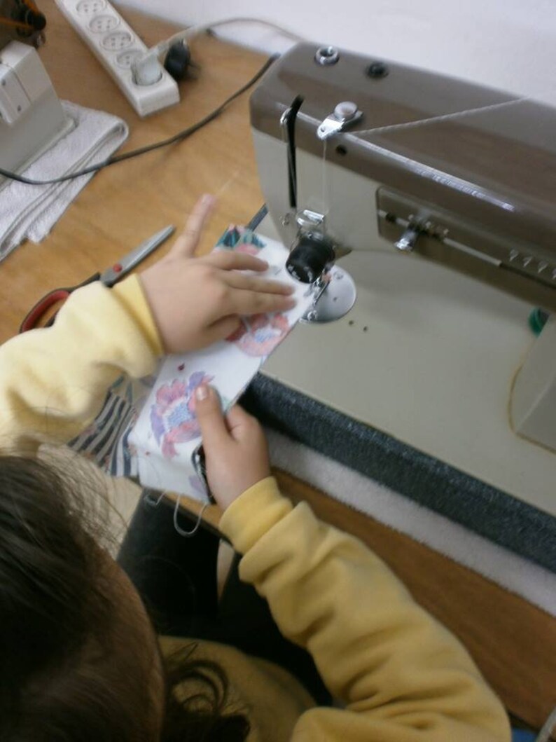 May include: A person is using a sewing machine to sew a piece of fabric. The fabric is colorful and has a floral pattern. The sewing machine is brown and has a white foot pedal.