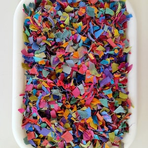 May include: A white tray filled with colourful fabric scraps. The scraps are various sizes and shapes, and they are arranged in a random pattern.