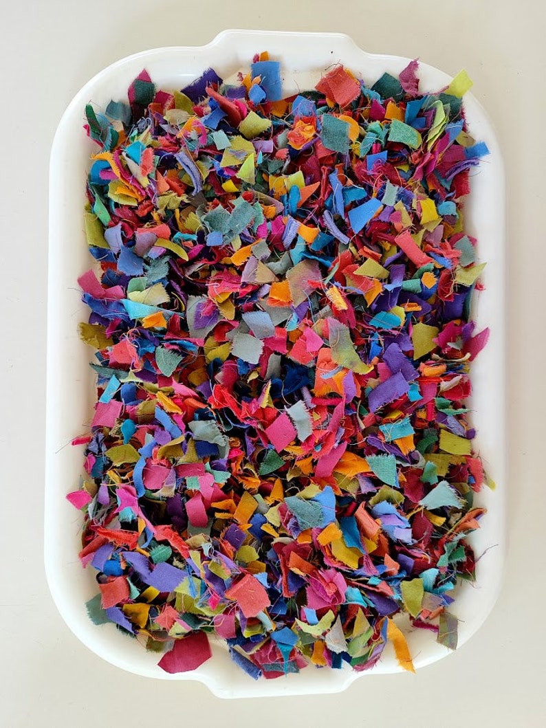 May include: A white tray filled with colourful fabric scraps. The scraps are various sizes and shapes, and they are arranged in a random pattern.