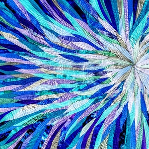 Op de afbeelding: Een kleurrijk abstract quilt met een uitbarsting van blauwe, turquoise, paarse en witte stofstroken die vanuit het midden naar buiten stralen.