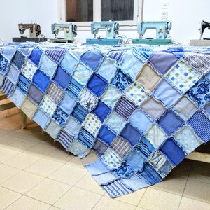May include: A blue and beige patchwork quilt made from squares of different fabrics. The quilt is draped over a table with four sewing machines in the background.