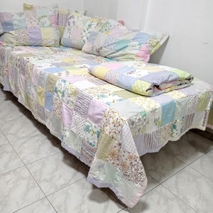May include: A patchwork quilt featuring a range of floral patterns in shades of pink, yellow, and blue. The quilt is crafted from various fabrics and textures, resulting in a distinctive and charming design.