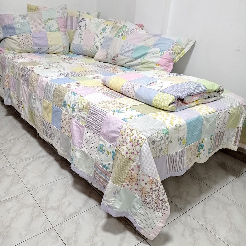May include: A patchwork quilt featuring a range of floral patterns in shades of pink, yellow, and blue. The quilt is crafted from various fabrics and textures, resulting in a distinctive and charming design.