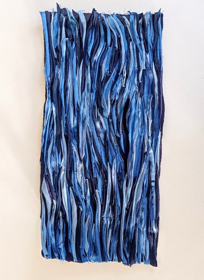 Puede incluir: Un tapiz de pared hecho de tiras de tela azul cosidas juntas. La tela es de varios tonos de azul, de claro a oscuro.