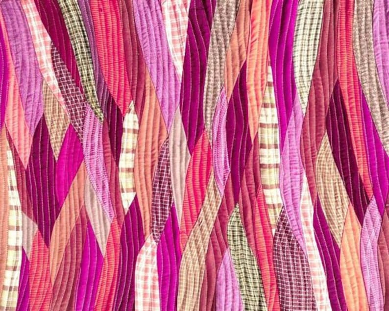 Op de afbeelding: Een quilt gemaakt van verschillende tinten roze, rood en bruin. De stof is in een golvend patroon aan elkaar gestikt.