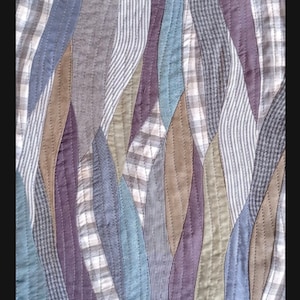 May include: A quilt made from various patterned fabrics in shades of blue, brown, grey, and purple. The fabric is sewn together in a wavy pattern.