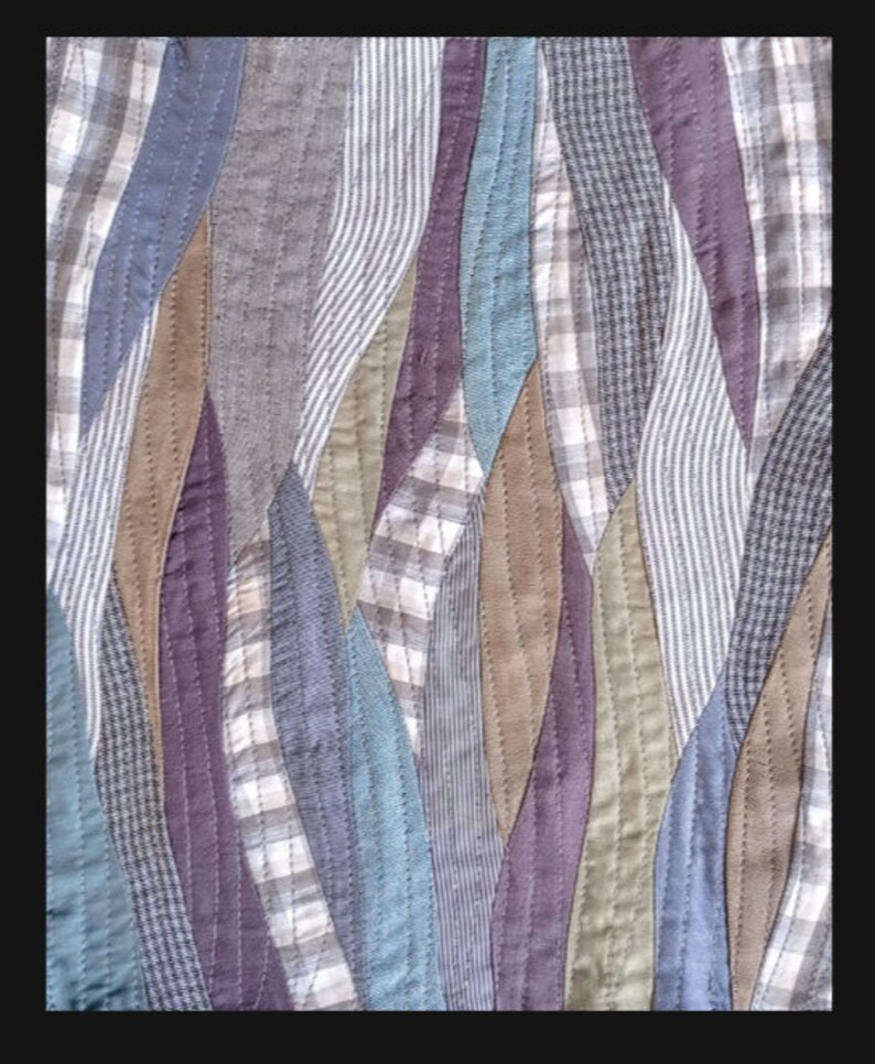 May include: A quilt made from various patterned fabrics in shades of blue, brown, grey, and purple. The fabric is sewn together in a wavy pattern.