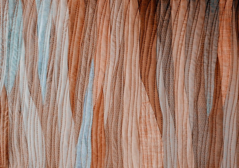 Peut inclure: Un gros plan sur un tissu matelass&eacute; avec un motif ondul&eacute; dans des tons de brun, beige et bleu.
