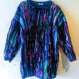 Puede incluir: Una camisa de manga larga azul, verde y morada con un dise&ntilde;o de patchwork. La camisa est&aacute; hecha de diferentes telas y tiene un patr&oacute;n abstracto &uacute;nico.