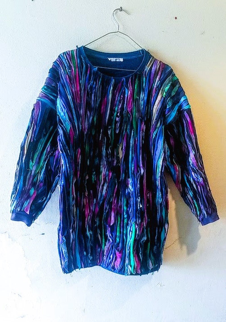 Puede incluir: Una camisa de manga larga azul, verde y morada con un dise&ntilde;o de patchwork. La camisa est&aacute; hecha de diferentes telas y tiene un patr&oacute;n abstracto &uacute;nico.