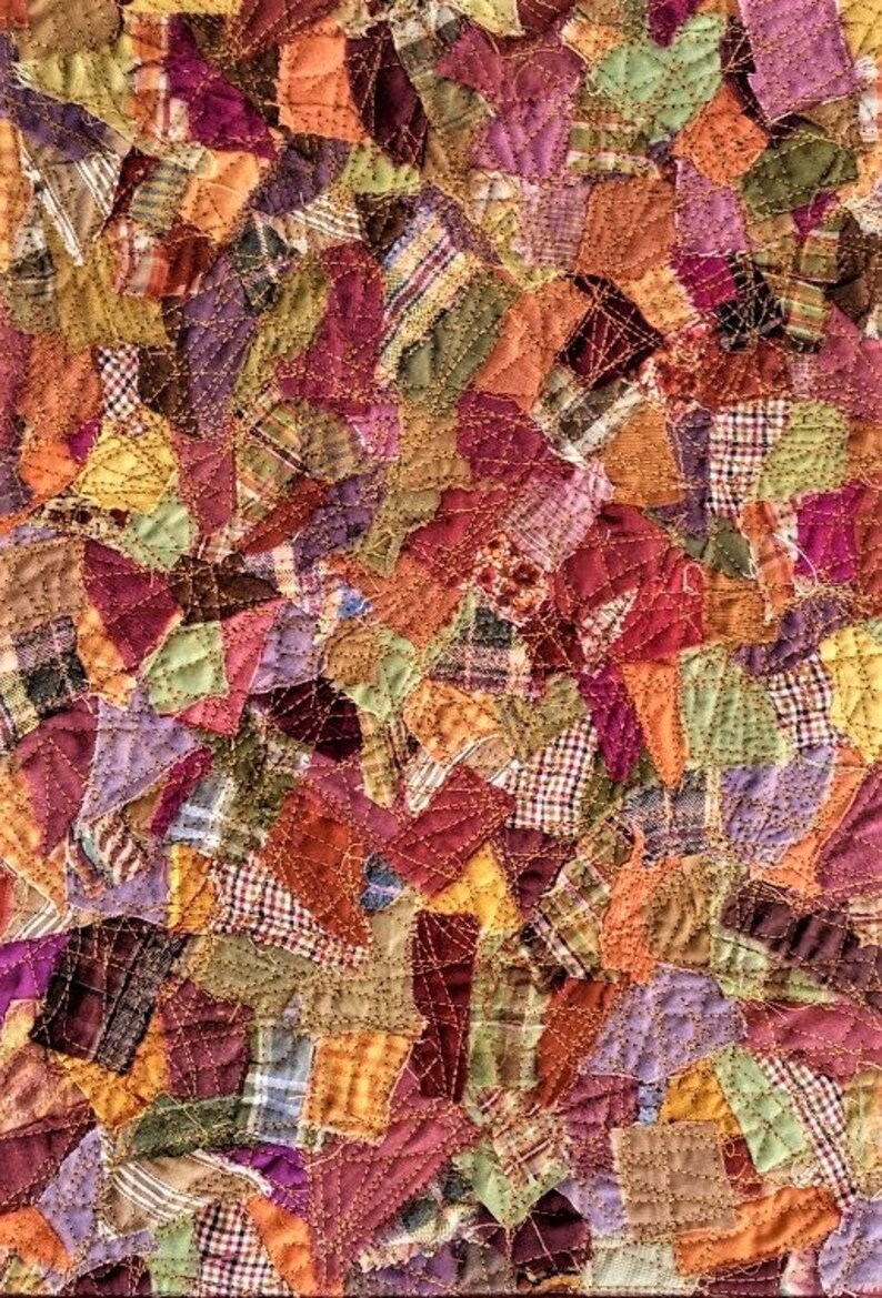 Op de afbeelding: Een patchworkdeken gemaakt van verschillende stoffen in tinten bruin, oranje, paars en groen. De deken is gemaakt van veel kleine stukjes stof die in een willekeurig patroon aan elkaar zijn genaaid. De deken is gequilt met een decoratieve steek.