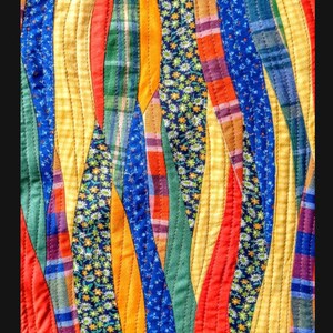 May include: A colourful quilt with a wavy pattern made from different fabrics. The quilt features a variety of colours, including red, yellow, blue, green, and white. The fabrics are arranged in a way that creates a sense of movement and energy.