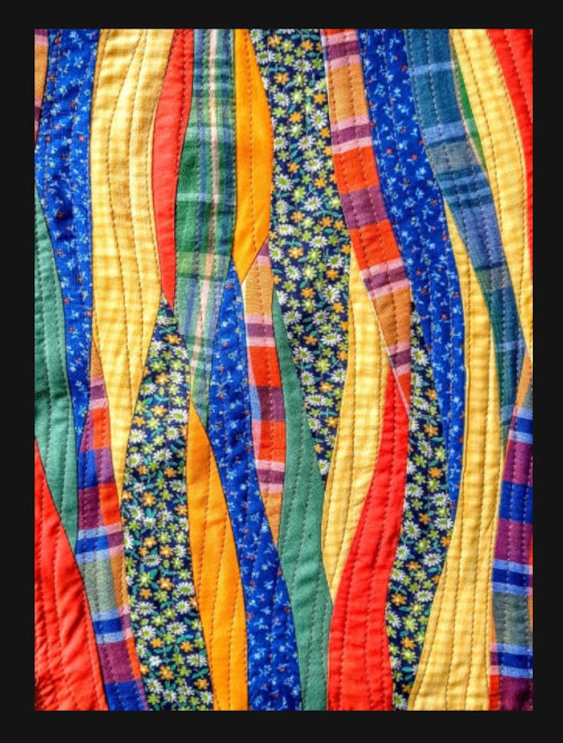 May include: A colourful quilt with a wavy pattern made from different fabrics. The quilt features a variety of colours, including red, yellow, blue, green, and white. The fabrics are arranged in a way that creates a sense of movement and energy.