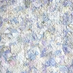 May include: A close-up of a quilt made from many small pieces of fabric in shades of white, blue, and purple. The fabric is sewn together in a patchwork pattern, creating a textured and intricate design.