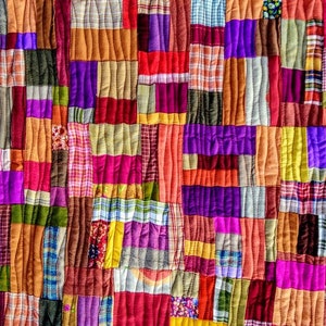 Pode incluir: Um cobertor de retalhos colorido feito de v&aacute;rios tecidos em tons de vermelho, laranja, roxo, marrom e verde. O cobertor &eacute; feito de quadrados e ret&acirc;ngulos de tamanhos diferentes, criando um padr&atilde;o visualmente interessante.