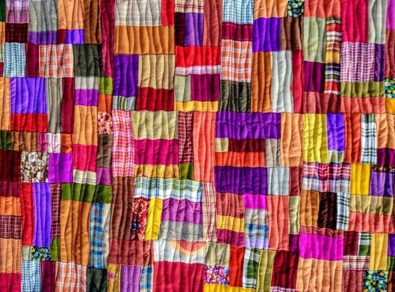 Pode incluir: Um cobertor de retalhos colorido feito de v&aacute;rios tecidos em tons de vermelho, laranja, roxo, marrom e verde. O cobertor &eacute; feito de quadrados e ret&acirc;ngulos de tamanhos diferentes, criando um padr&atilde;o visualmente interessante.